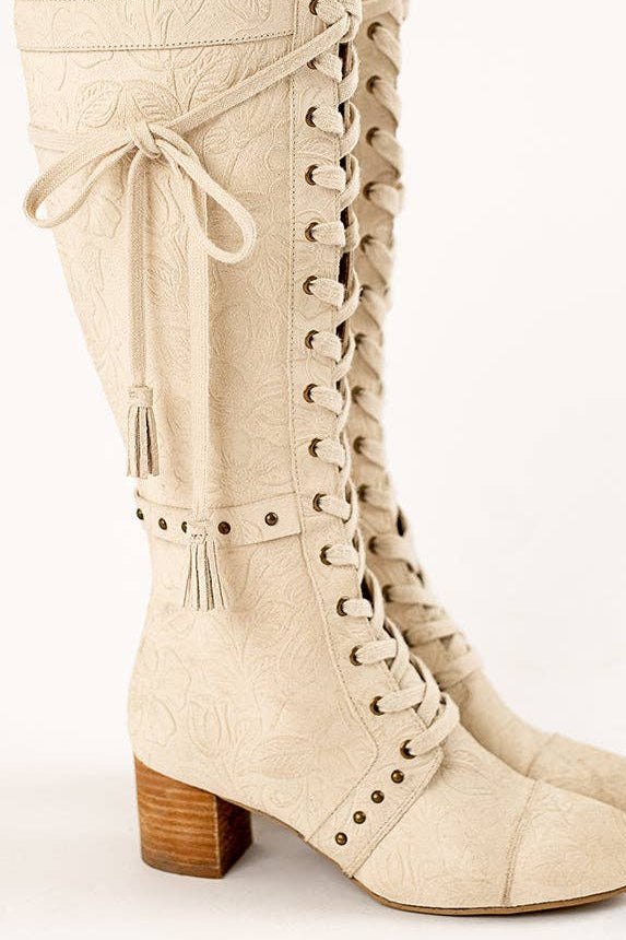 Beige knee-high boots with lace-up design and wooden heel on a white background
