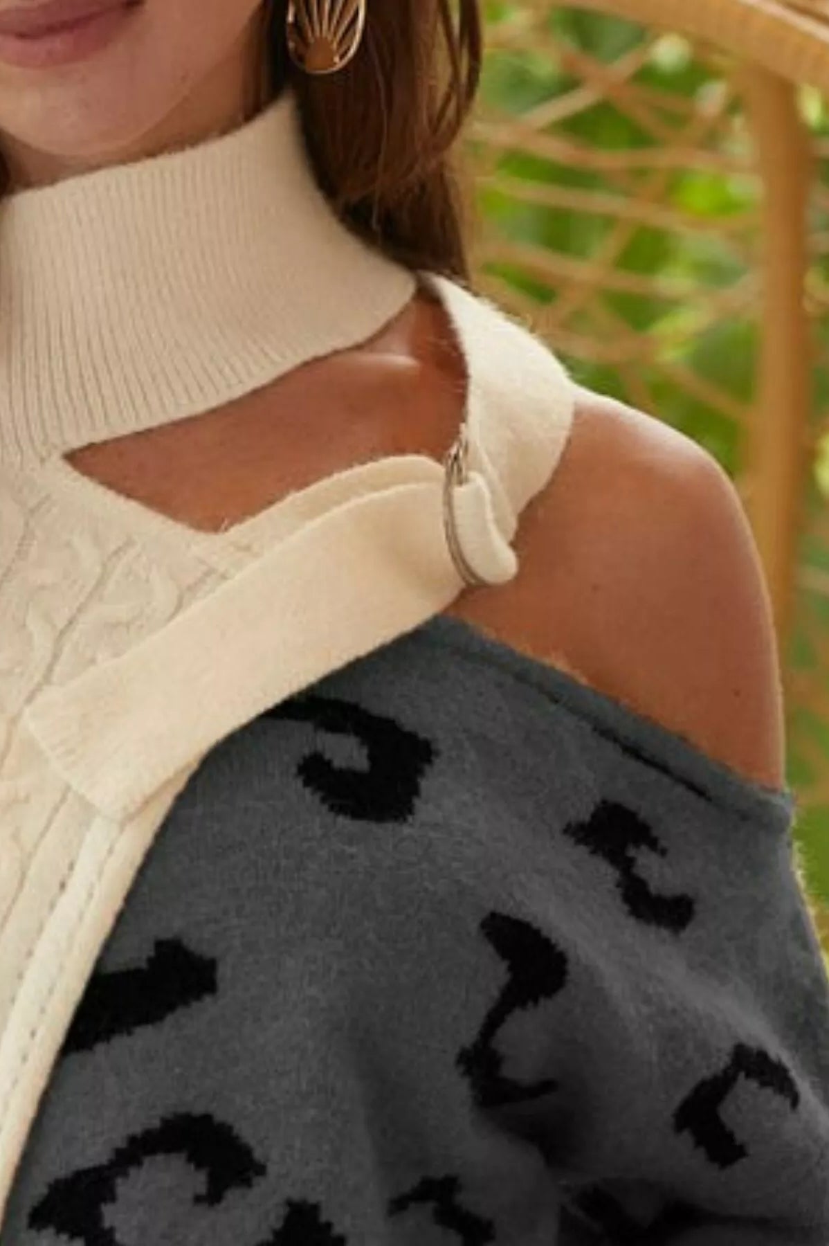 Person wearing a cream sweater with a cut-out design, holding a dark gray sweater with black patterns.