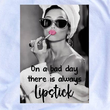 White t-shirt with graphic design and text on a wooden surface, accompanied by black and white earrings.