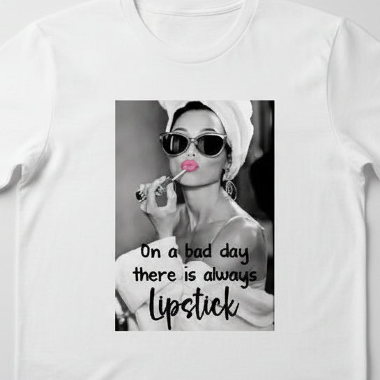 White t-shirt with graphic design and text on a wooden surface, accompanied by black and white earrings.