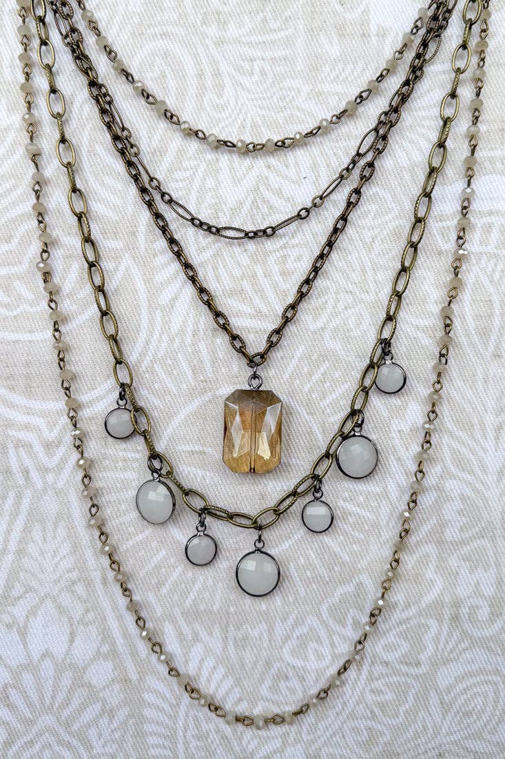 Layered chain necklaces with beads and a central pendant on a textured white background