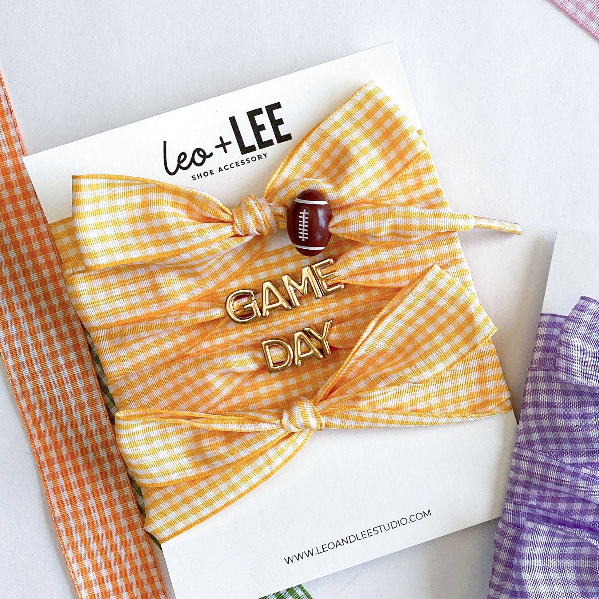 Two hair bow pins with 'Game Day' text on cards, surrounded by colorful ribbons.