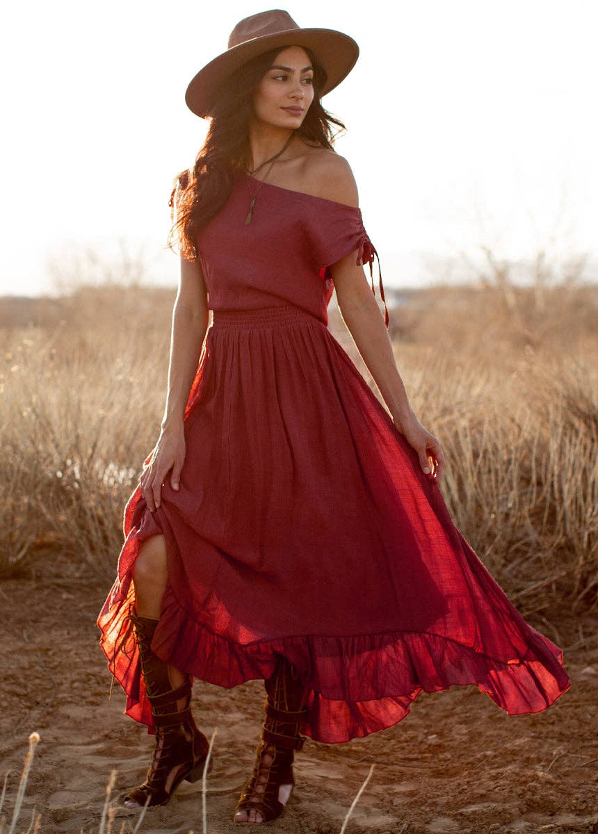 Woman in a red dress and hat standing in a field with sunset lighting
