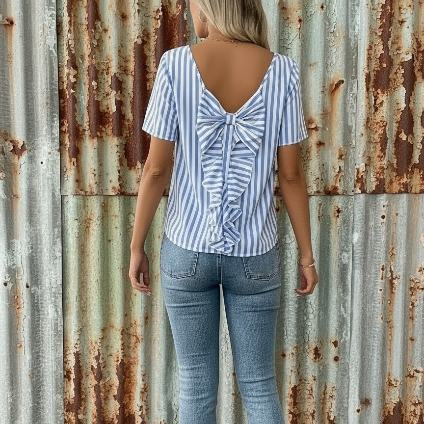 Woman wearing a blue and white striped blouse with a bow detail, standing in a casual setting.