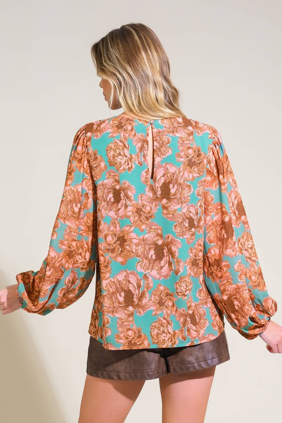 Woman wearing a floral blouse with long sleeves on a plain background