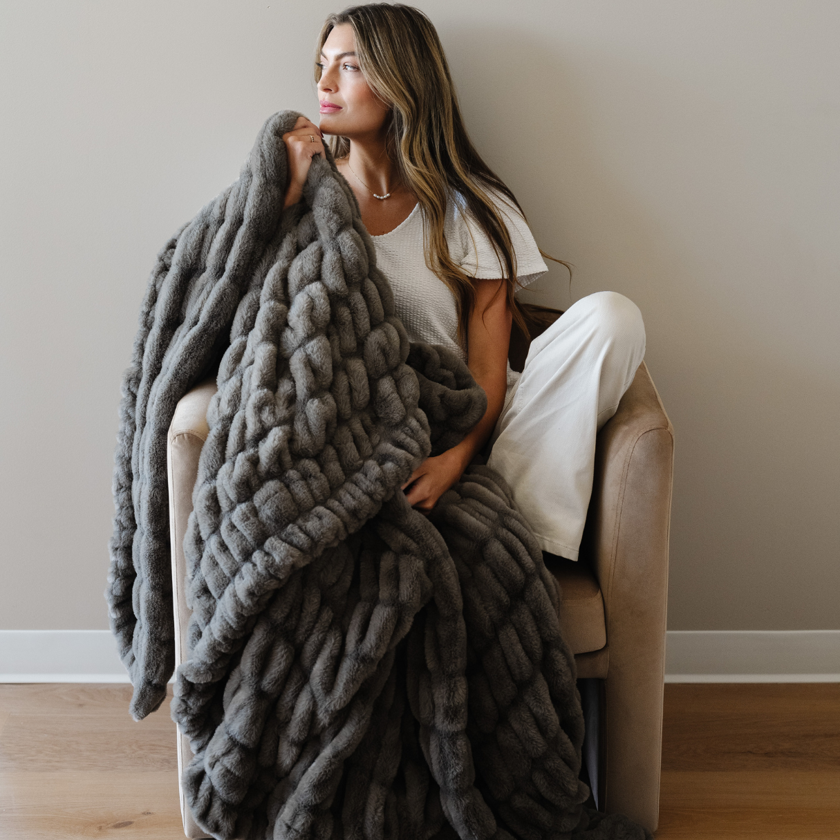 Woman sitting on a chair with a large gray knitted blanket draped over her