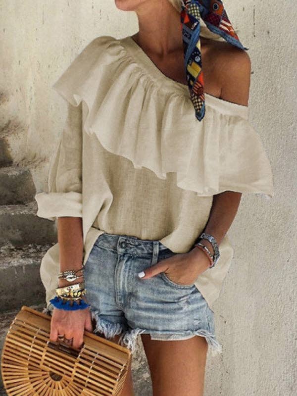 Woman wearing a beige off-shoulder top and denim shorts, holding a woven bag.