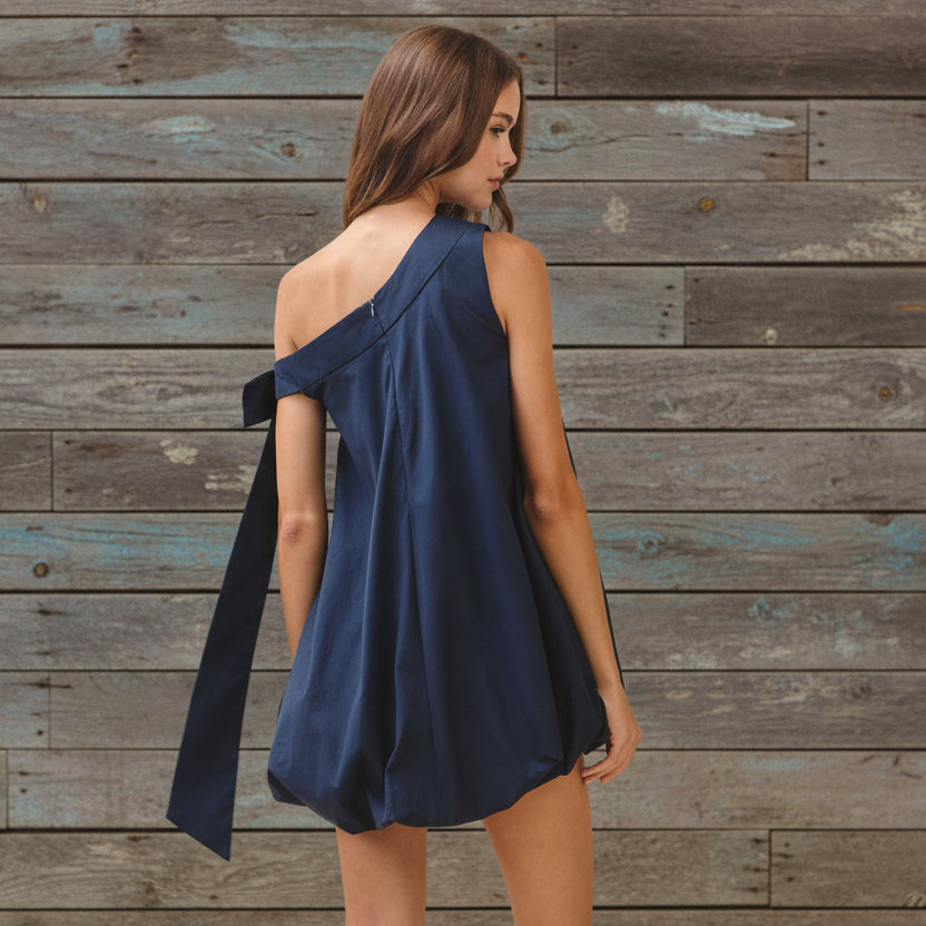 Woman wearing a navy blue one-shoulder dress on a beige background