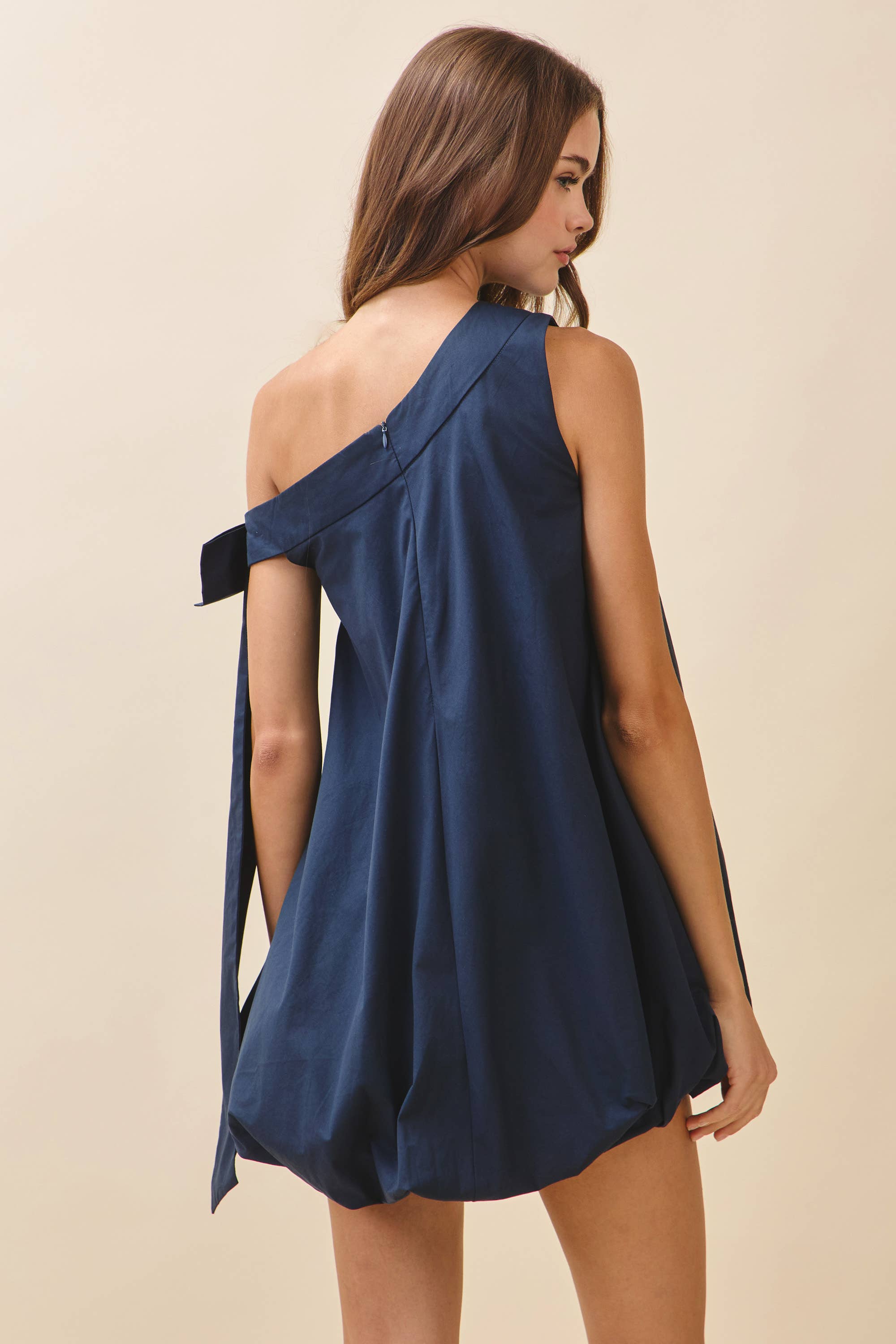 Woman wearing a navy blue one-shoulder dress on a beige background