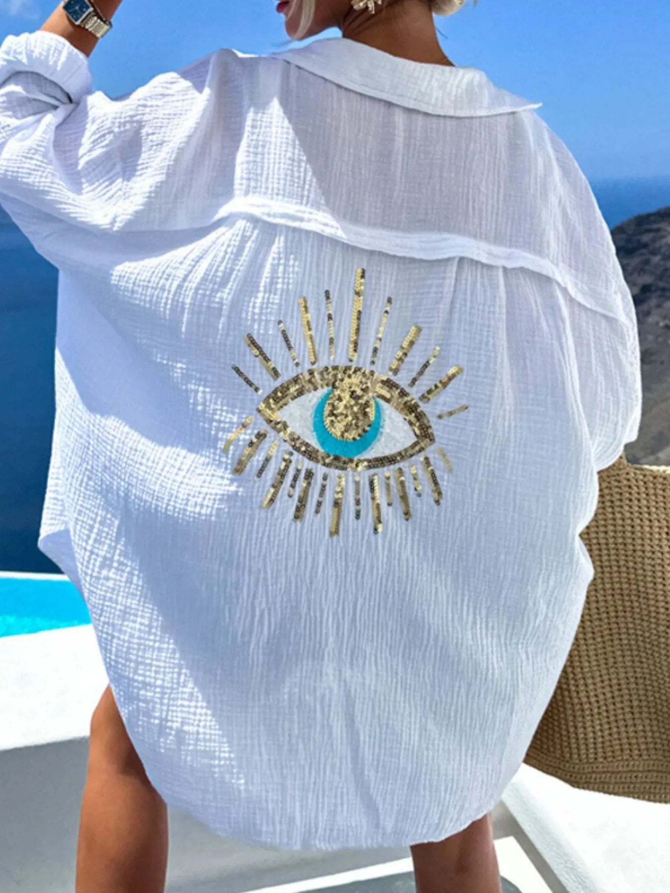 White embroidered cover-up with eye design by a pool
