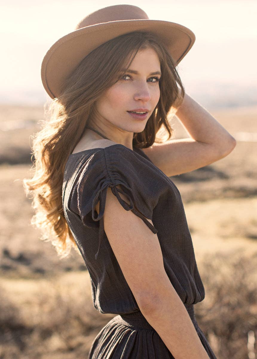 Woman wearing a beige hat and dark dress in a desert setting