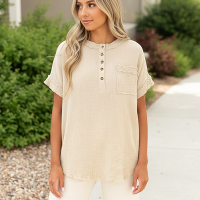 Beige short-sleeve top worn by a person with a blurred green background