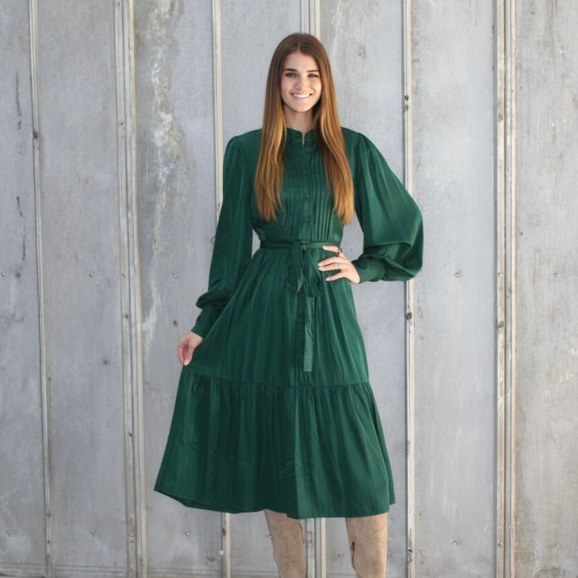 Woman wearing a green dress standing against a gray concrete wall.