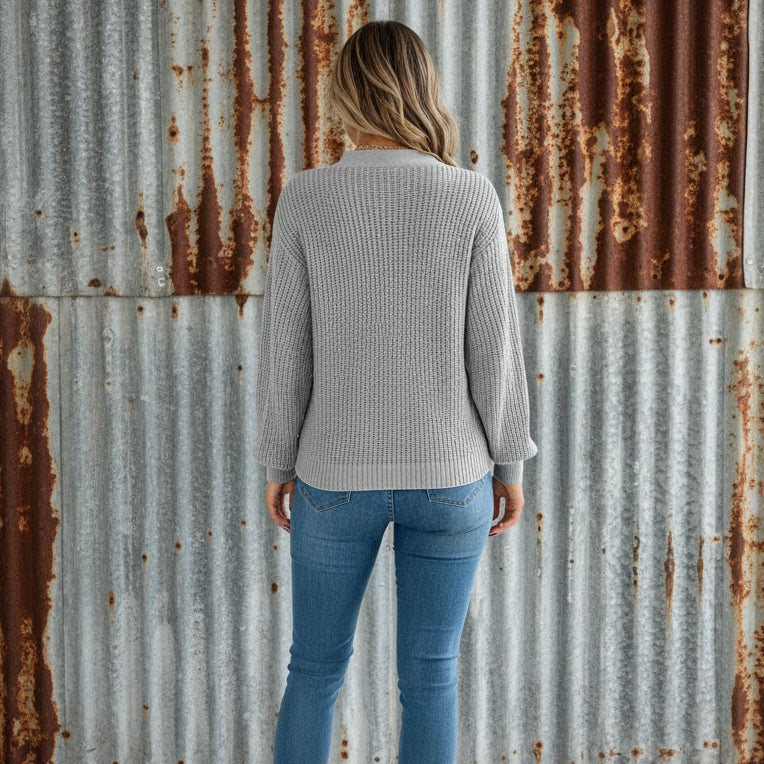 Person wearing a gray knitted sweater and blue jeans against a white background