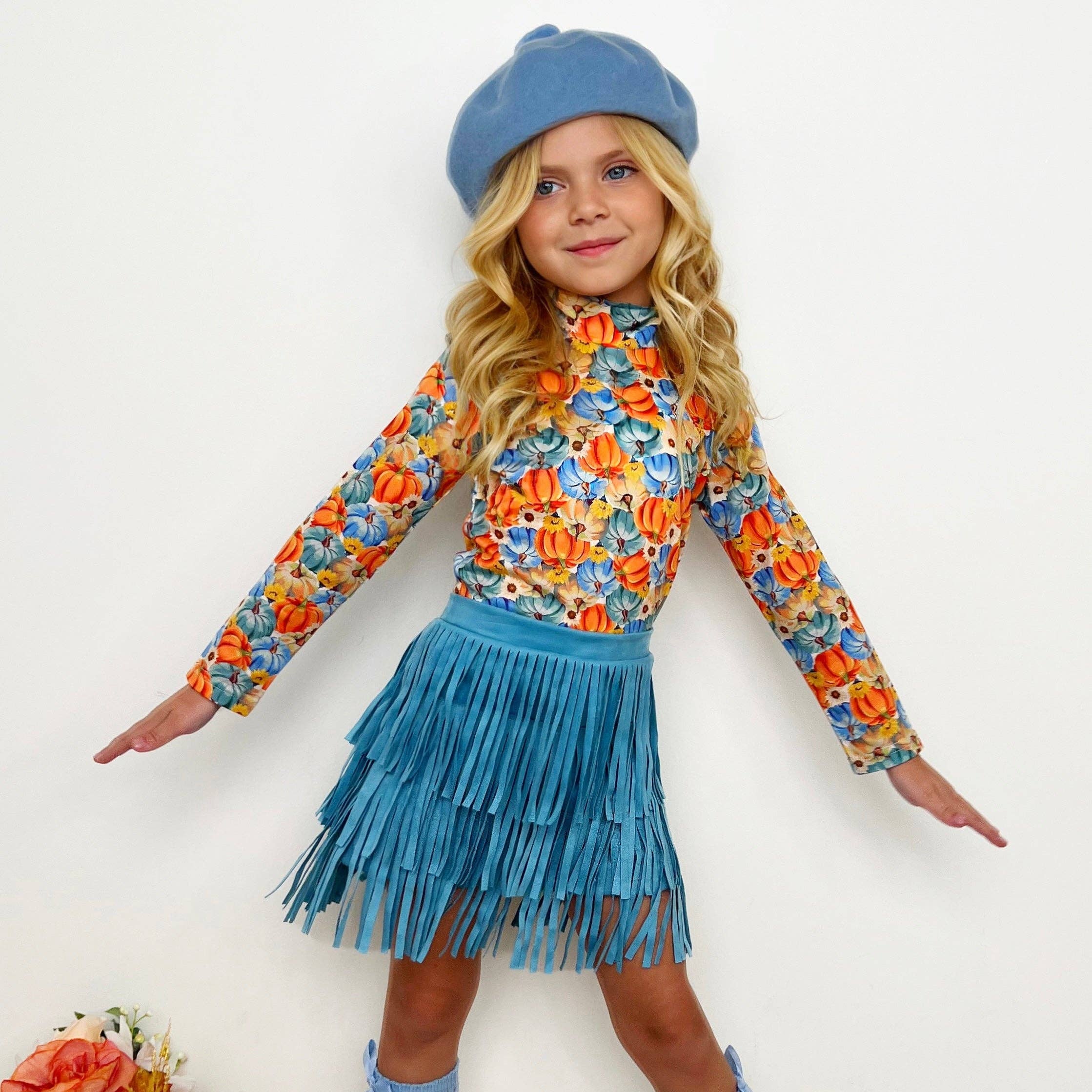 Young girl in a floral top and blue fringed skirt with beige boots on a white background