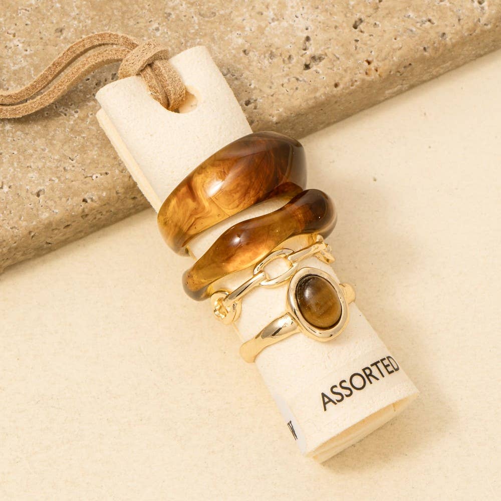 Assorted jewelry including rings and a necklace on a beige surface with a cork stopper.