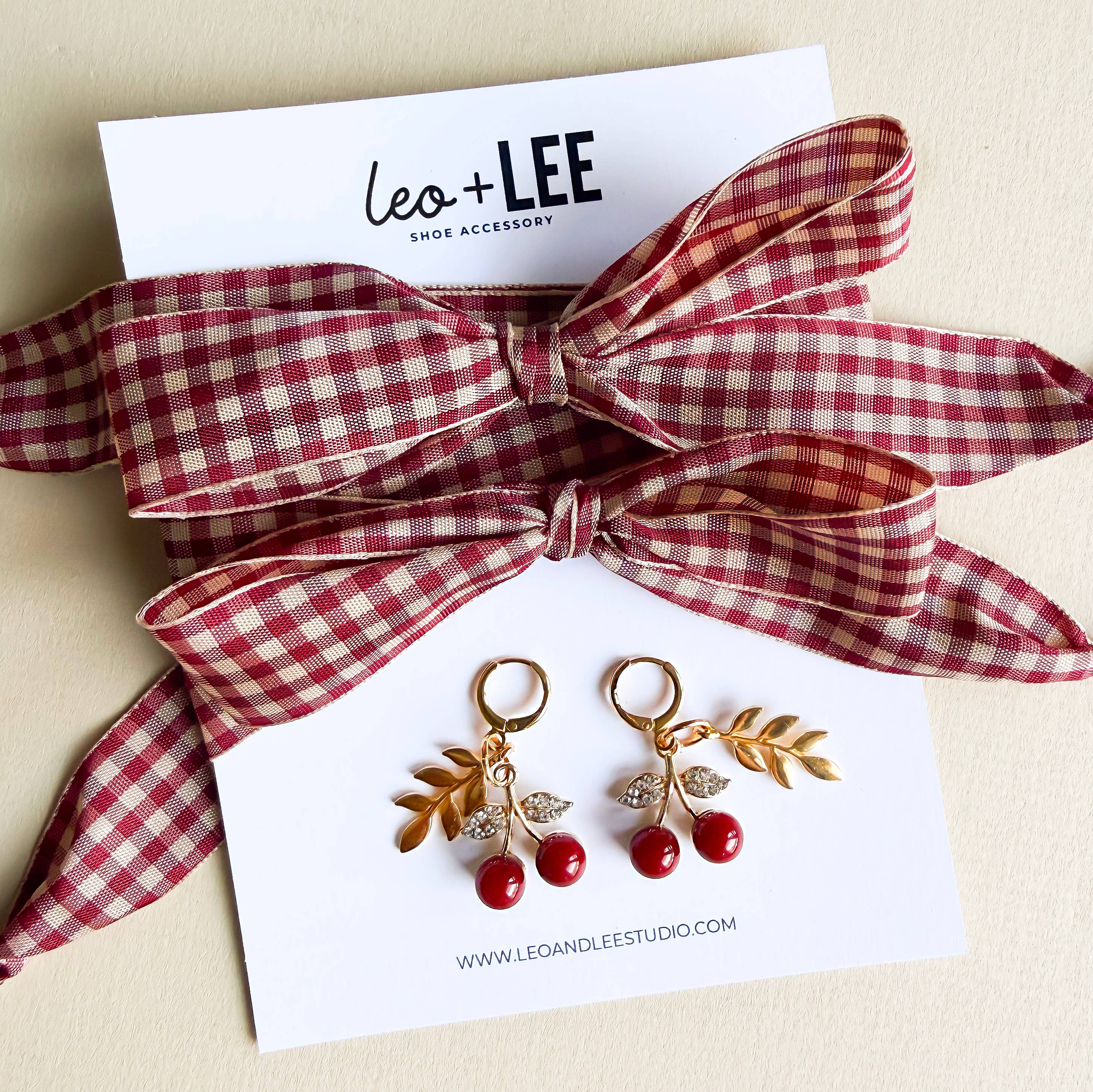 Pair of cherry-themed earrings with a red and white checkered bow on a card with 'Leo+Lee' branding.