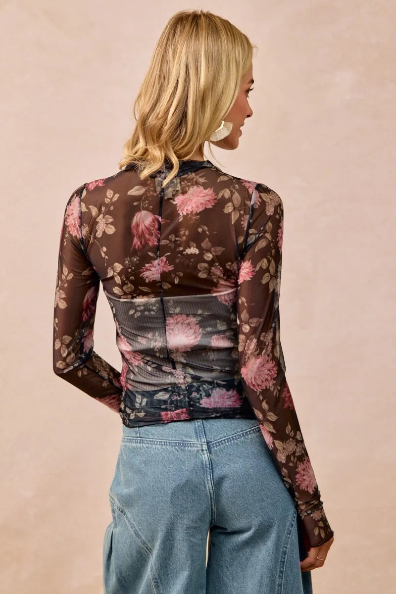 Woman wearing a floral sheer top with long sleeves against a beige background