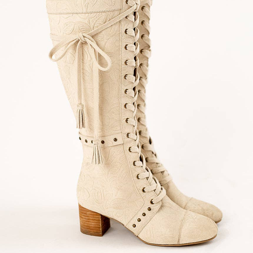 Beige knee-high boots with lace-up design and wooden heel on a white background