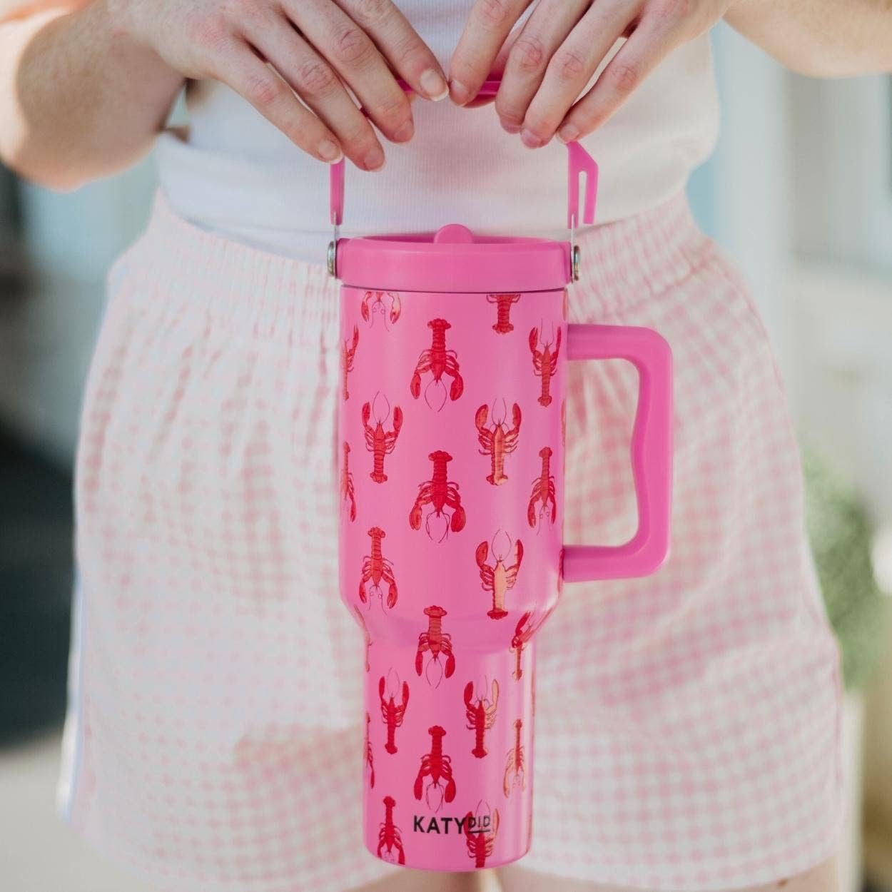 Pink tumbler with lobster pattern held by a person wearing a white shirt and pink shorts.