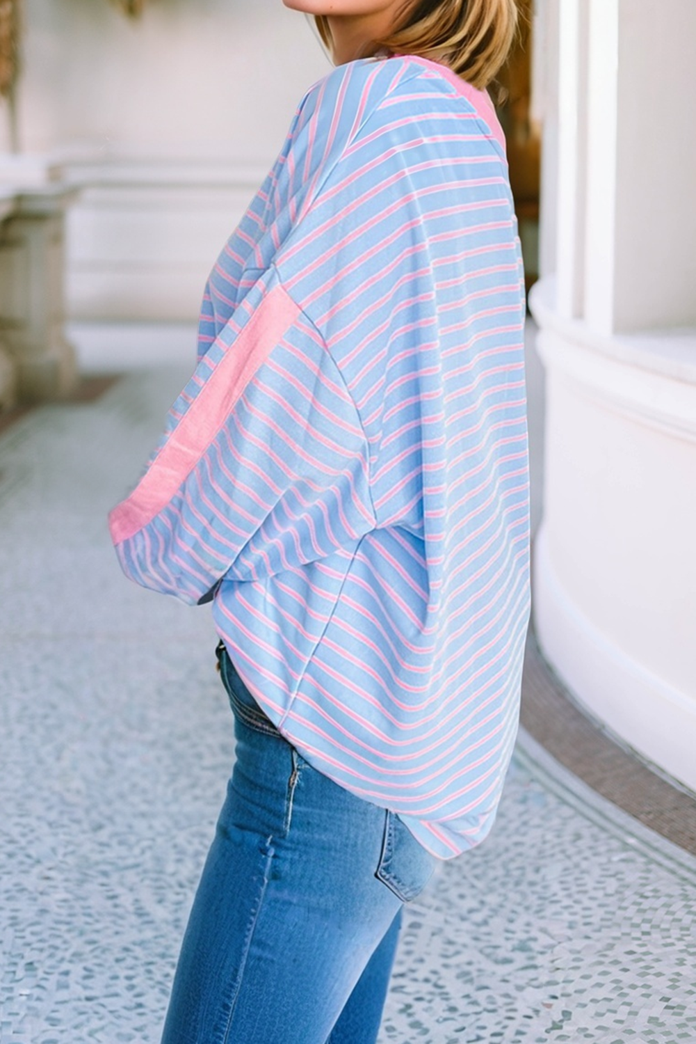 Person wearing a light blue and pink striped shirt with jeans, standing on a stone path.
