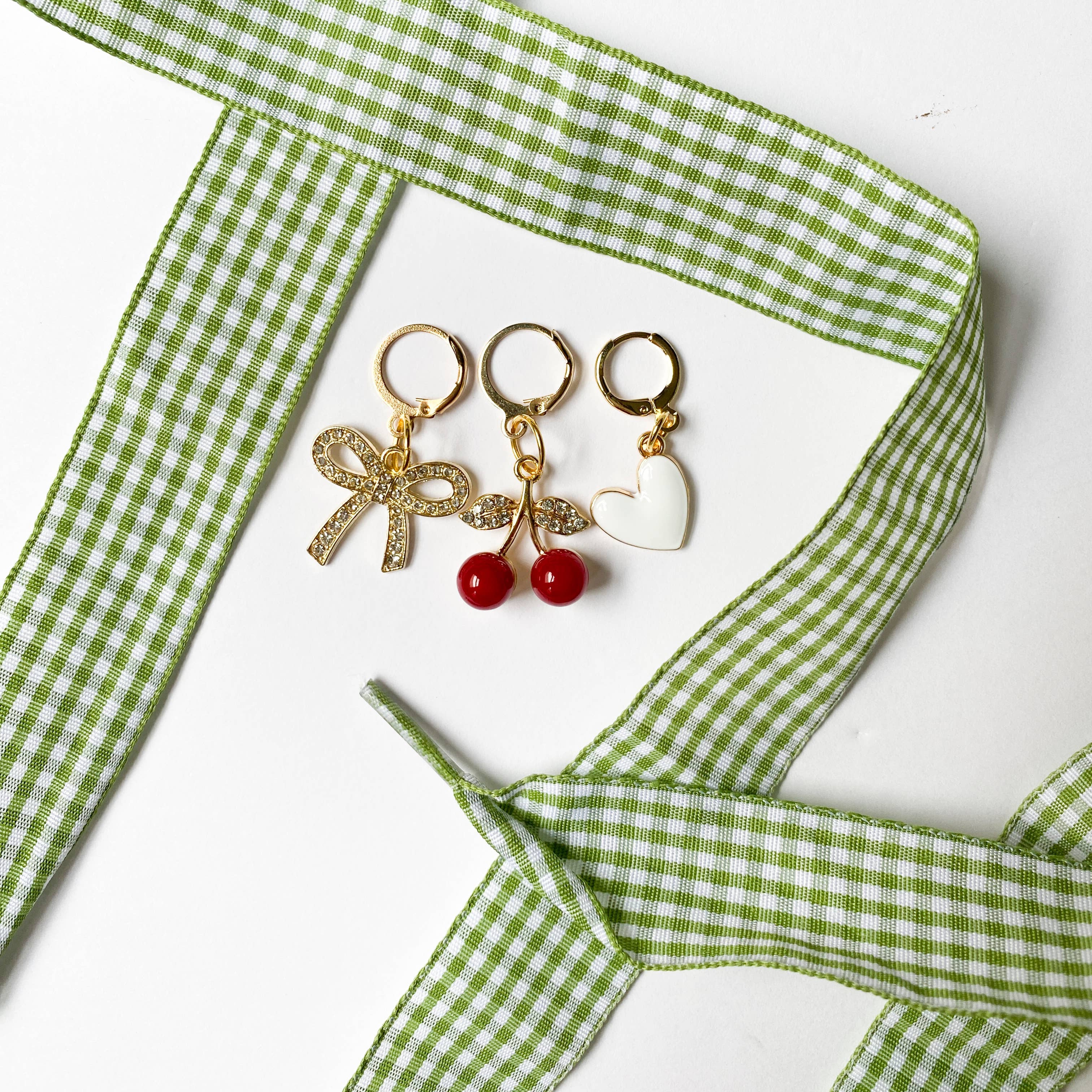 Three pairs of earrings with decorative elements on a green checkered ribbon.