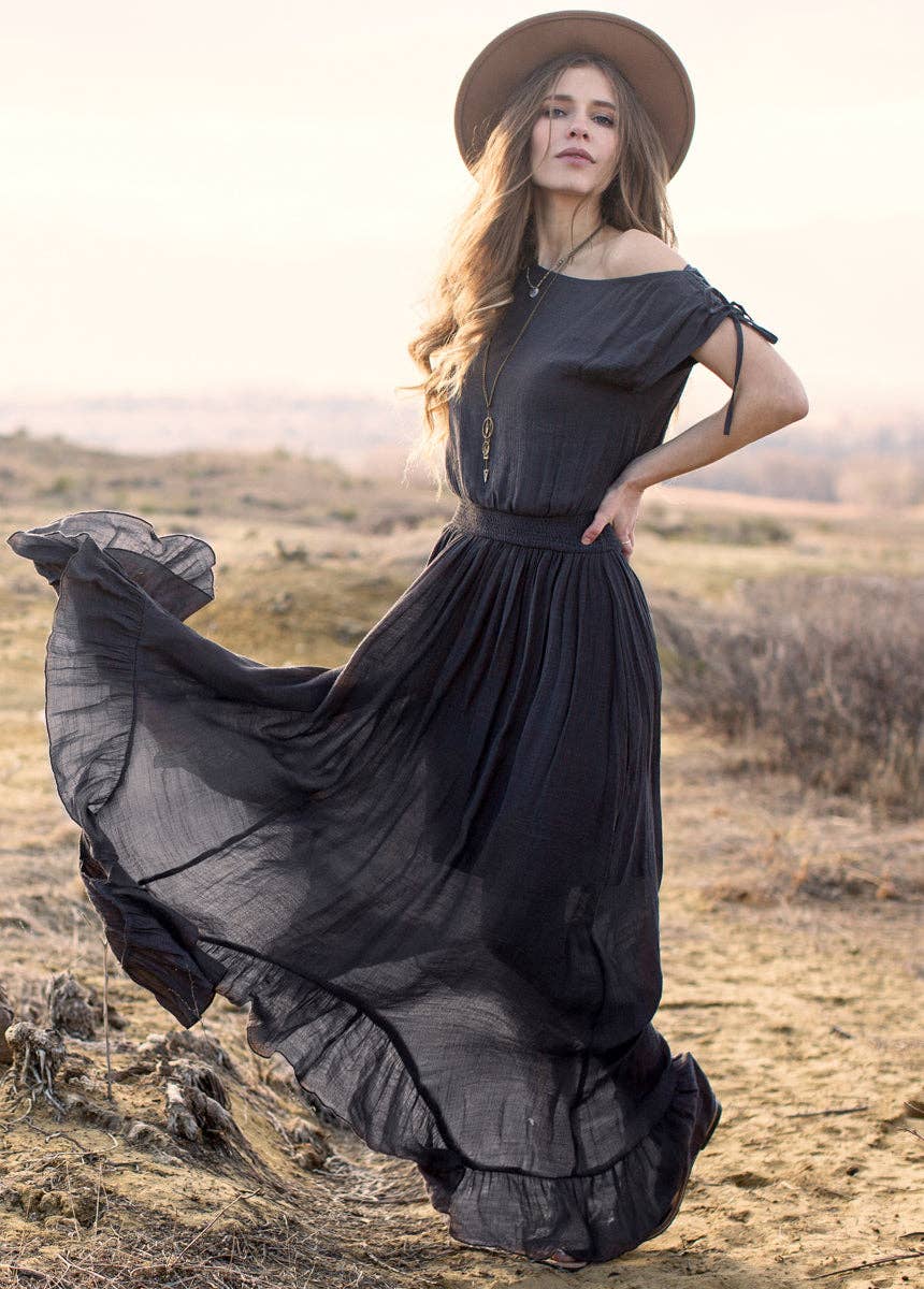 Woman in a long black dress and hat standing in a desert landscape