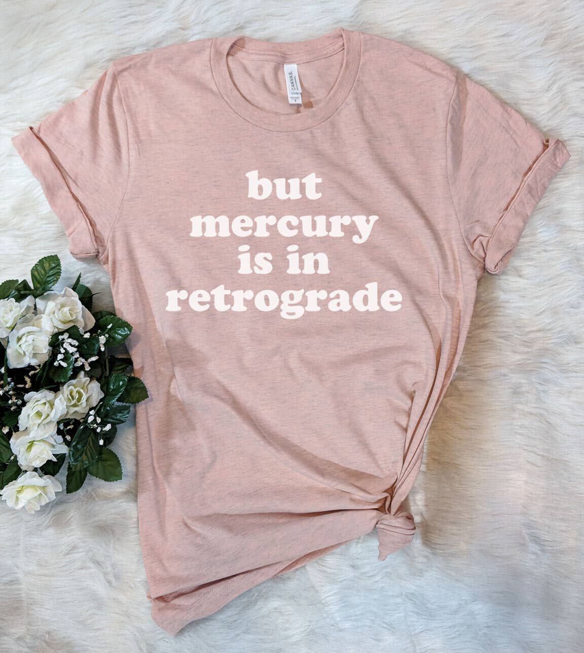 Pink t-shirt with 'but mercury is in retrograde' text on a white fur background with flowers.