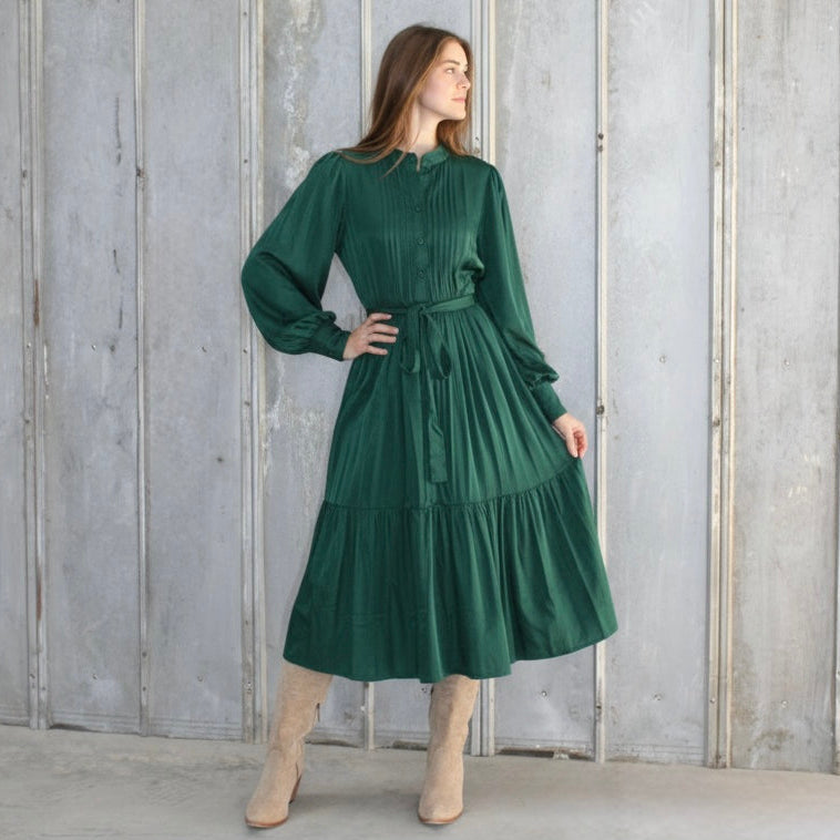 Woman wearing a green dress standing against a gray wooden panel background