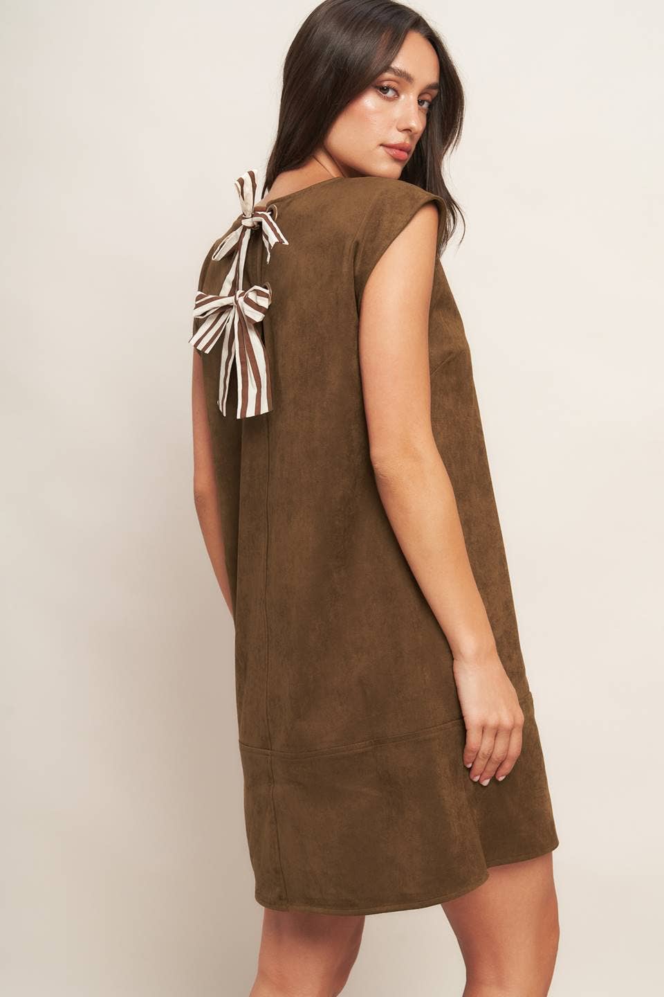 Woman wearing a brown dress with a bow detail on a plain background