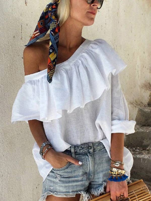 Woman wearing a white off-shoulder top with ruffles and denim shorts against a neutral background.