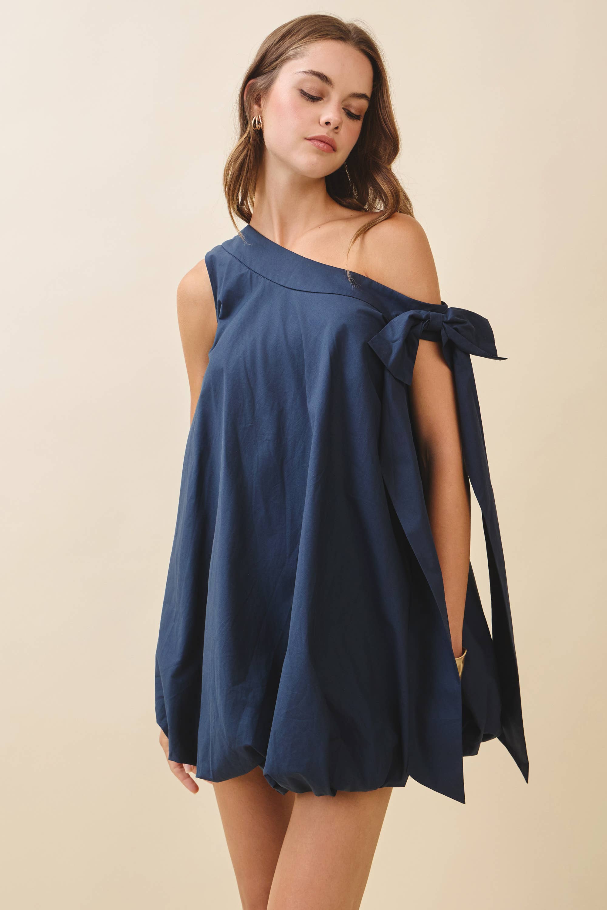 Woman wearing a navy blue off-shoulder dress with a bow detail on a beige background