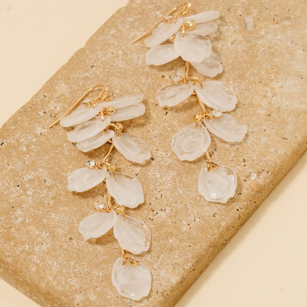 Gold and clear stone earrings on a beige stone surface