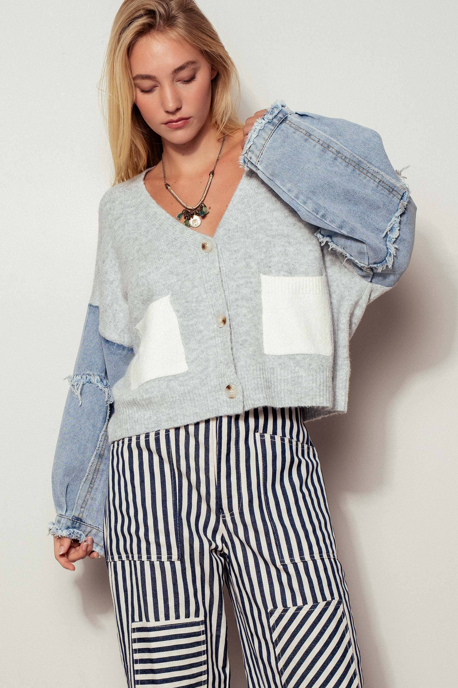 Woman wearing a gray cardigan with denim sleeves and striped pants against a white background