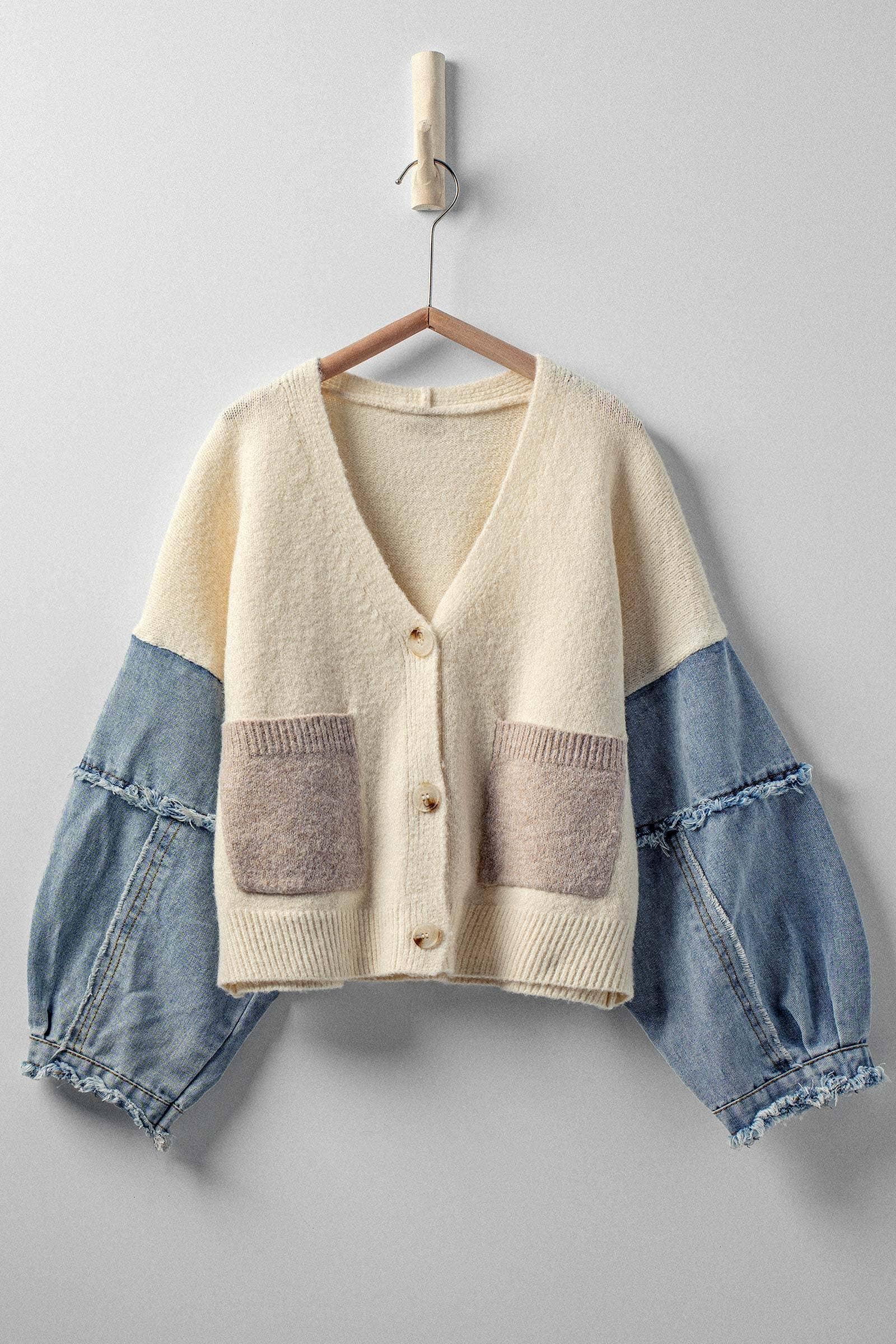 Cardigan with denim sleeves and front pocket on a hanger against a gray background