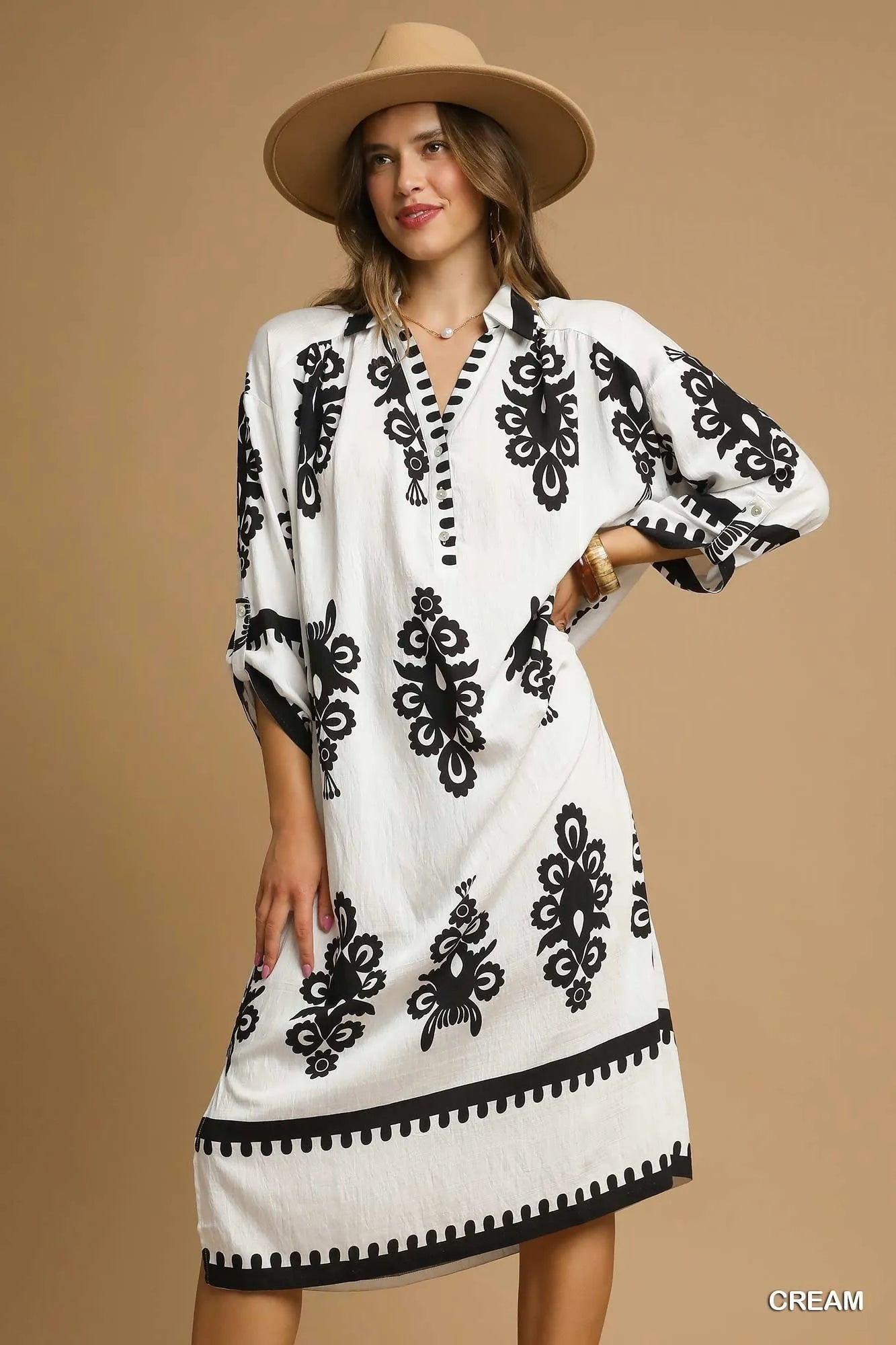 Woman wearing a white dress with black patterns and a beige hat on a beige background
