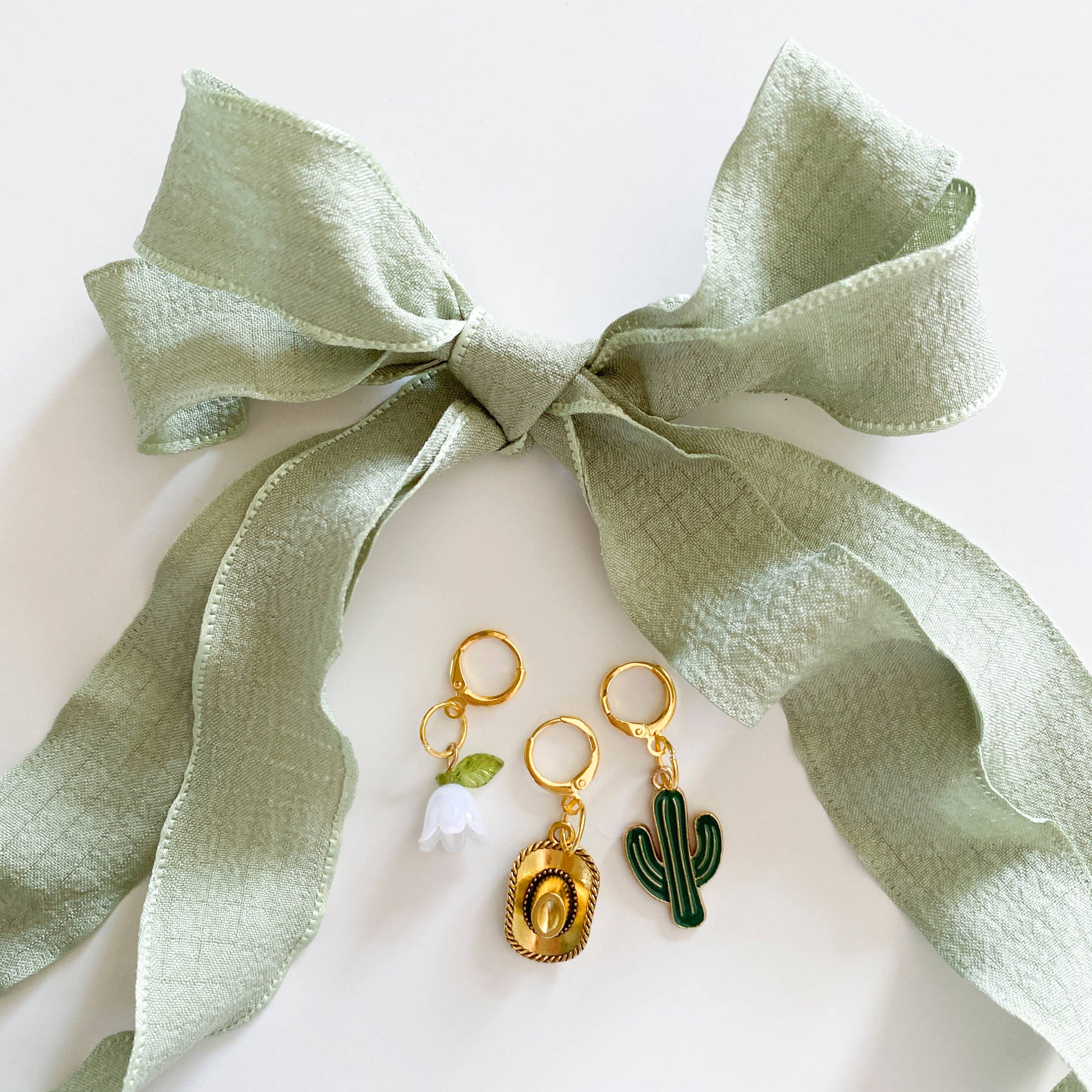 Two gold earrings with green accents on a white stand with a green ribbon.