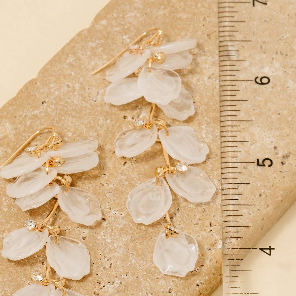Pair of floral earrings with gold accents on a textured surface next to a ruler.