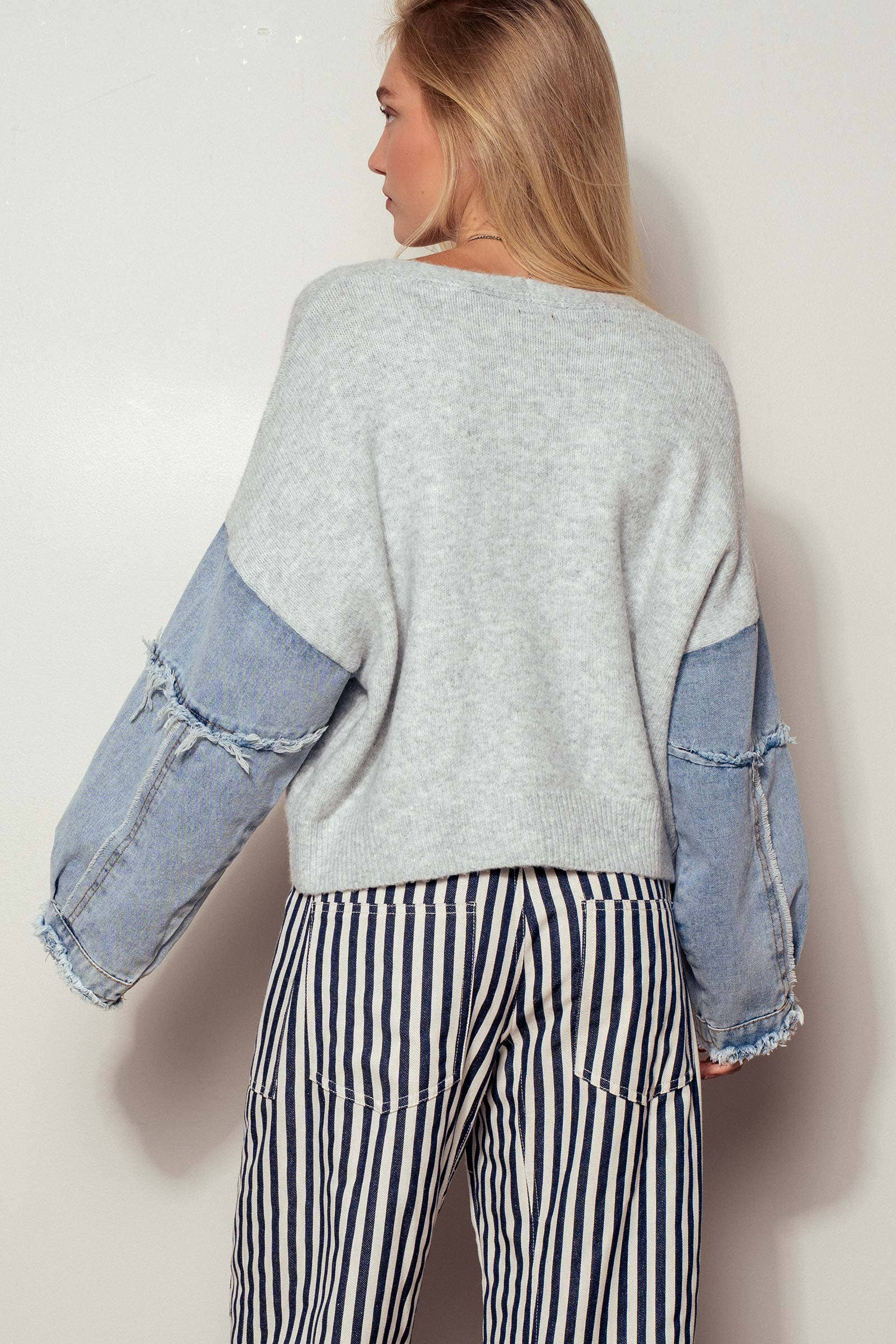 Person wearing a gray sweater with denim sleeves and striped pants against a white background