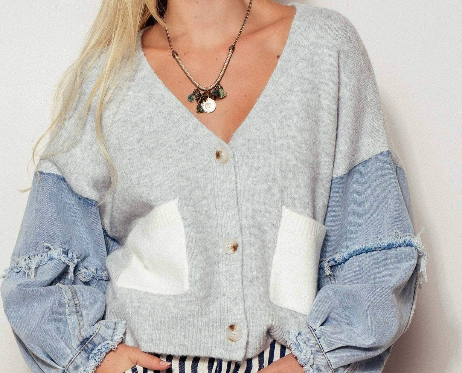 Woman wearing a gray and blue cardigan with white patches on a plain background