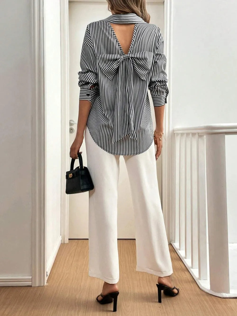 Woman wearing a striped shirt with a bow detail and white pants, holding a black handbag.