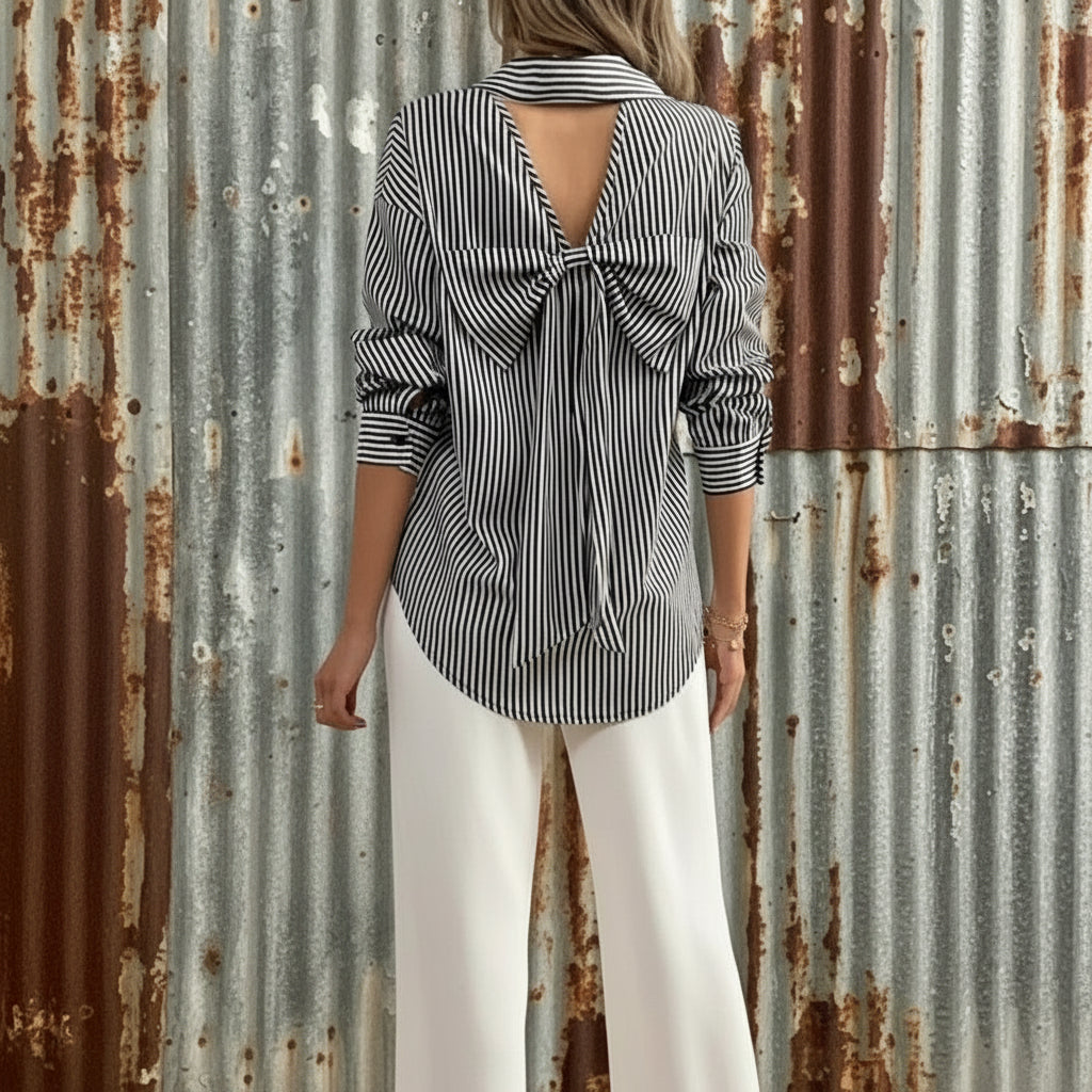 Woman wearing a striped shirt with a bow detail and white pants, holding a black handbag.