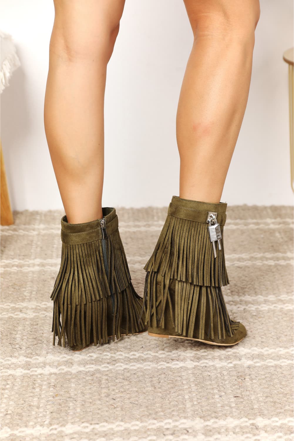 Green fringe boots worn by a person on a neutral background