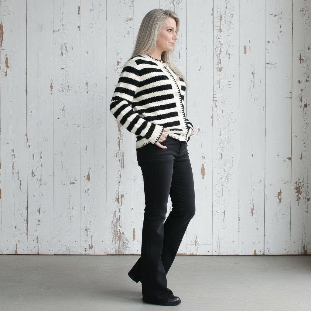 Person wearing a black and white striped sweater and black pants leaning against a wall.