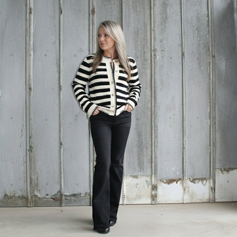Person wearing a black and white striped sweater and black pants leaning against a wall.