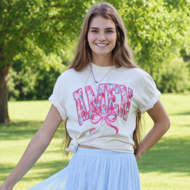 Woman wearing a graphic t-shirt and light blue skirt standing on grass with trees in the background