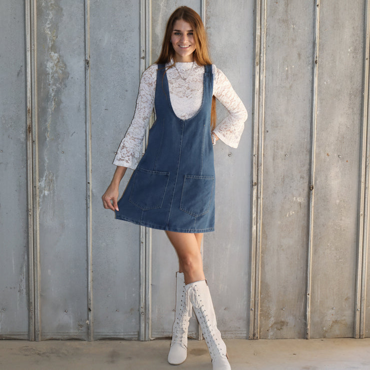 Person wearing a denim dress and white boots on a concrete staircase.
