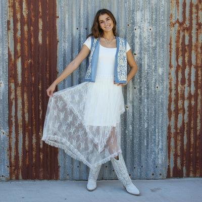 Woman in a white dress with blue accents standing on a brick pavement.