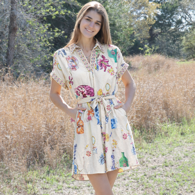 Woman in a floral dress standing in a natural setting with trees and grass.