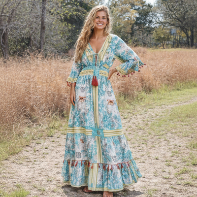 Woman in a long, patterned dress standing in a natural setting with trees and grass.